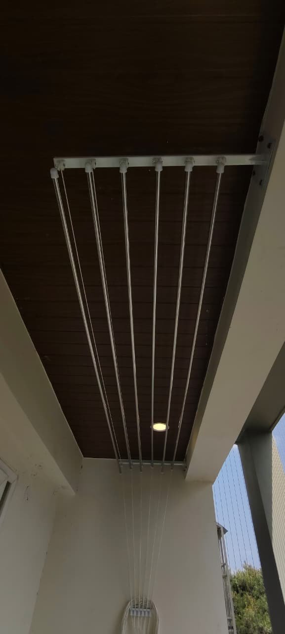 Ceiling cloth hanger rods under a warm-lit dark wooden balcony ceiling