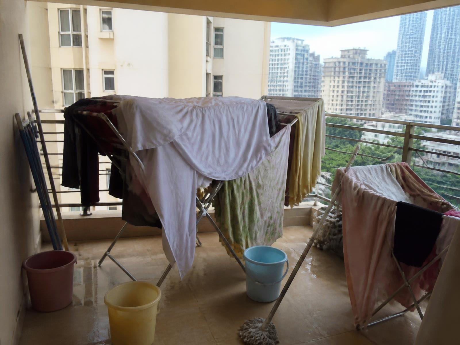 Large balcony cluttered with two drying stands and buckets before installation